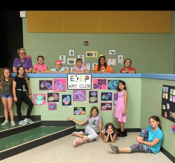 students and teacher stand in front of artwork wall